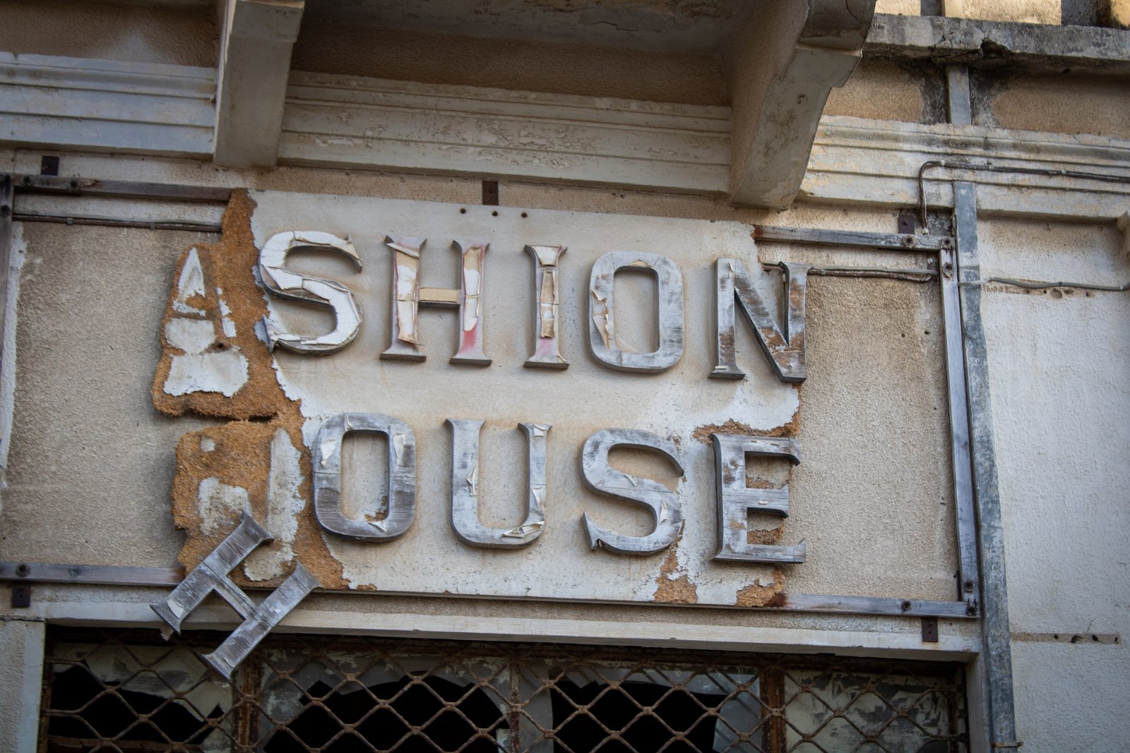 Изронен надпис „Fashion House“ над изоставен магазин във Вароша