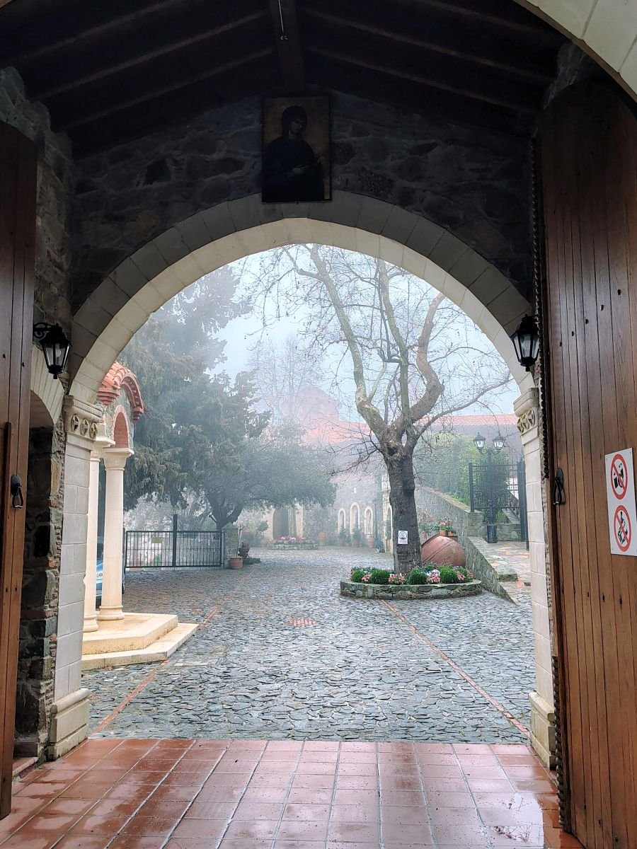 Поглед през входната арка към двора на манастира Махерас в мъгла